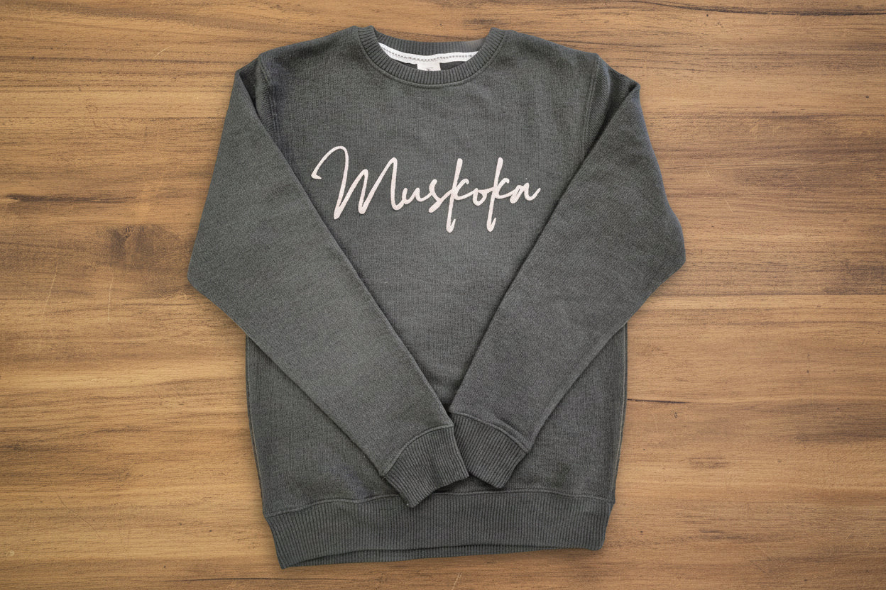 Dark gray sweatshirt with 'Muskoka' text on a wooden surface