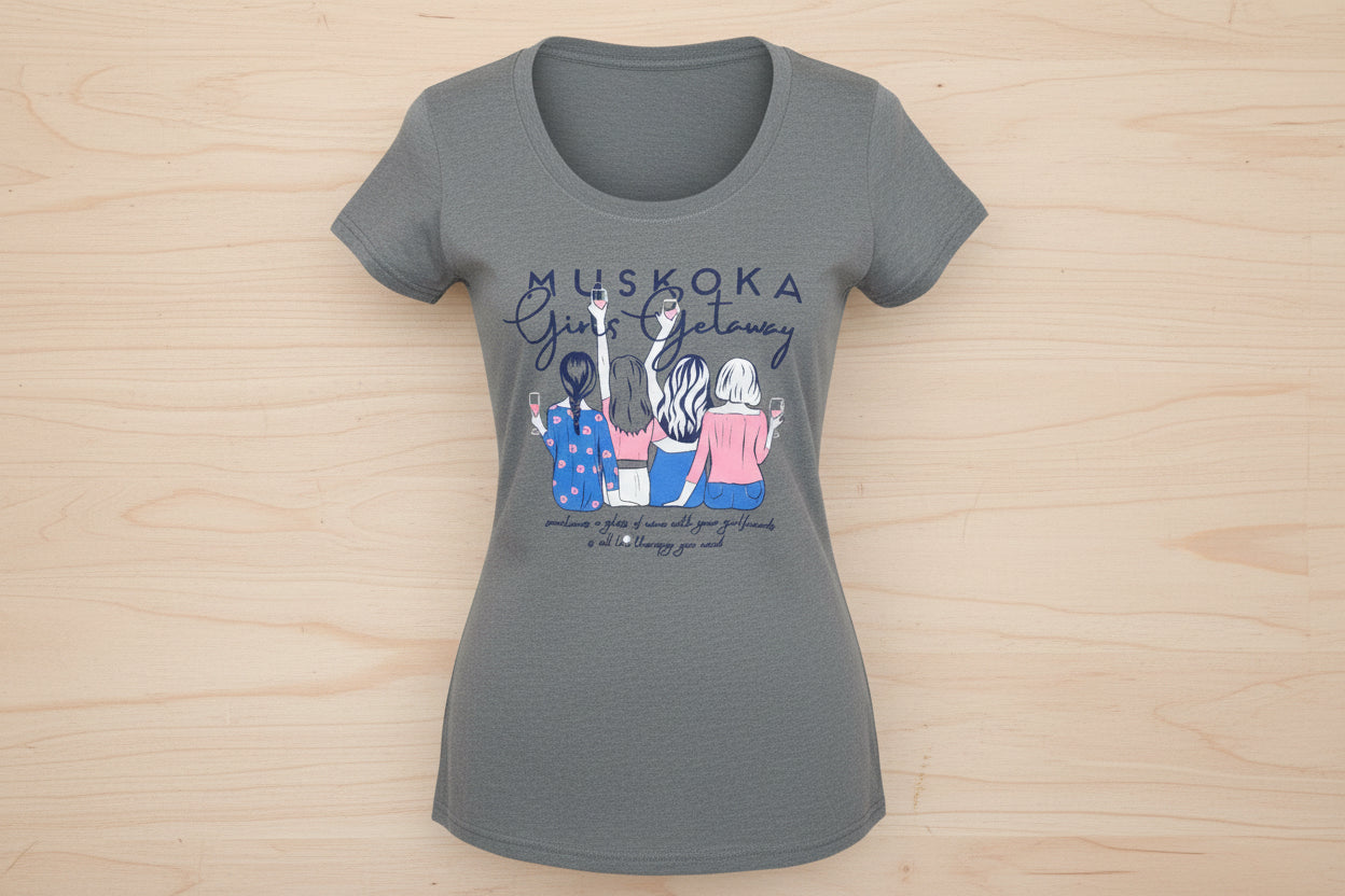 A gray t-shirt with text 'MUSKOKA Girls Getaway' and an illustration of three women wearing hats and holding coffee cups.